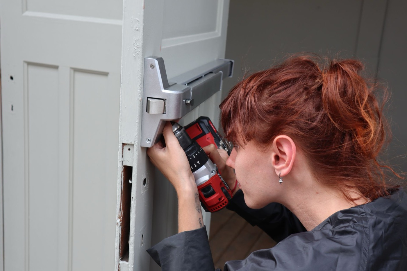 Technician installing a new lock mechanism on a door edge with a power drill